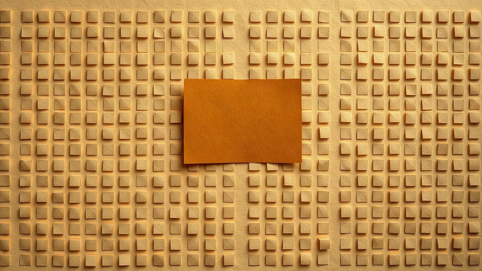 A dense grid of small tobacco-brown paper rectangles on a warm sand ground, one of them lifted clear of the grid in ochre